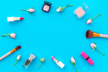 Rose, pink decorative cosmetics frame. Lipstick, bulk, eyeshadow and small rose flowers on blue background top view copy space