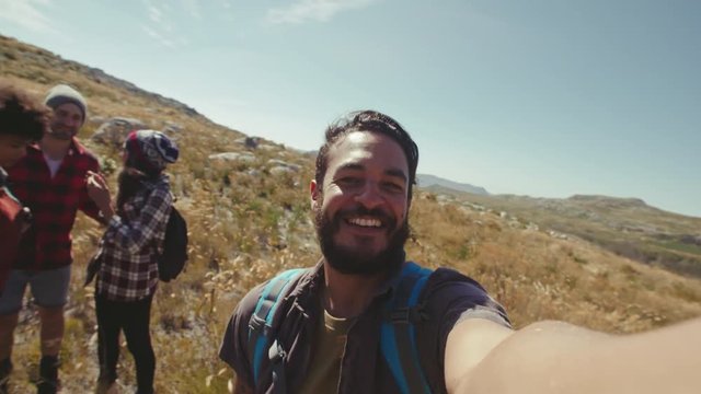 Young man taking selfie with friends during a hike. Man filming funny moments of friends during a country walk.