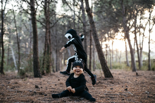 Cute baby in black bat costume against running skeleton kid in f