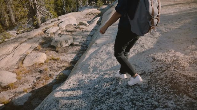 Camera follows young tourist girl hiking alone with backpack on amazing white rock at Yosemite park USA slow motion.