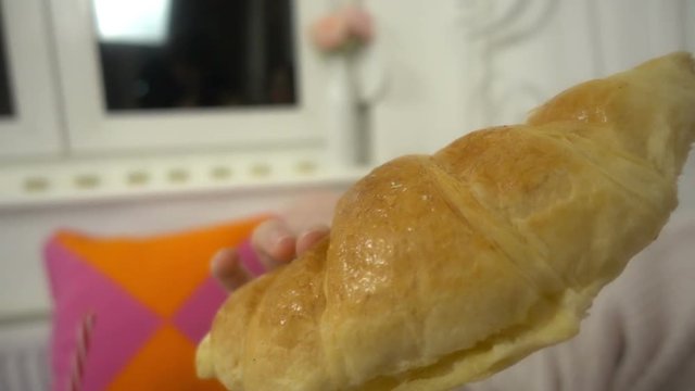 Young beautiful girl eats a croissant. Closeup slow motion of warm relaxing moments.