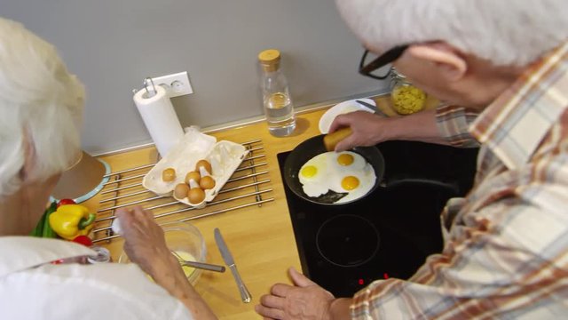 Back view of old woman and old man cooking breakfast together in kitchen