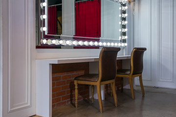 Beautiful interior of modern makeup room for beauty fashion with mirror lights illumination and white counter, wooden chairs vintage style decoration contemporary
