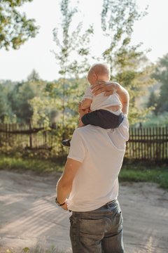 Back view portrait of father carrying his son on shoulders and holding him with hand