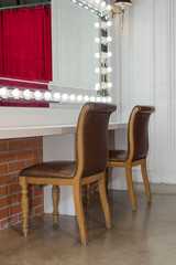 Beautiful interior of modern makeup room for beauty fashion with mirror lights illumination and white counter, wooden chairs vintage style decoration contemporary
