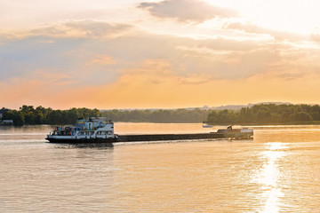 tugboat pushes barge with sand in the river at sunset