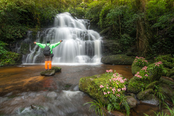 Tourist standing in front of Mun Daeng waterfalls and pink snapdragon flowers growth in rainforest of Phu Hin Rong Kla national park, Phitsanulok province of Thailand.