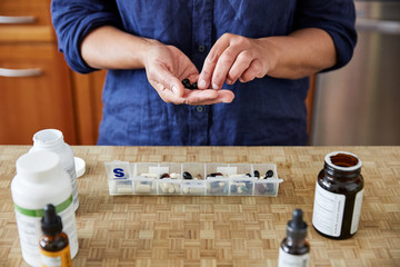 Close-up of mature woman organizing her health supplements and medications in the kitchen 