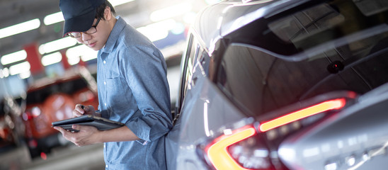 Young Asian auto mechanic holding digital tablet checking car in auto service garage. Mechanical maintenance engineer working in automotive industry. Automobile servicing and repair concept