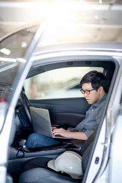 Male Asian mechanical engineer or auto mechanic using laptop computer on driver seat in the car. Automobile industry and technology concept.