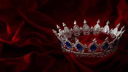 Queen coronation in fairy tales and legends monarchy and royal jewels concept with close up on a sparkling silver crown or tiara on low key dark red velvet background with copy space