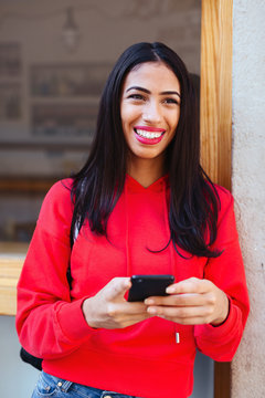 Smiling woman wearing red sweater using her phone in the city.