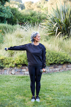 Mature woman with grey hair lifting weights and working out in backyard