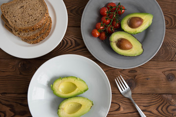 Preparing and cooking healthy avocado sandwich on dark rye toast bread made with fresh avocado paste, cherry tomatoes on brown wooden background