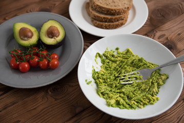Preparing and cooking healthy avocado sandwich on dark rye toast bread made with fresh avocado paste, cherry tomatoes on brown wooden background