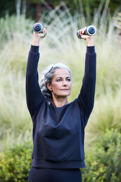 Mature woman with grey hair lifting weights and working out in backyard