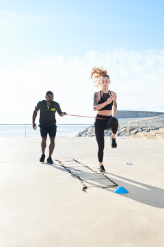 Personal trainer holding stretching rope while sportswoman runni