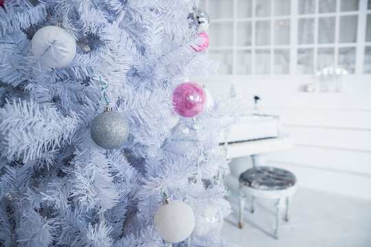 White Christmas tree decorated with silver and pink ornaments at the piano background.Winter scene. New Year decoration.Xmas interior design includes decorated Christmas tree.Selective focus.Classical