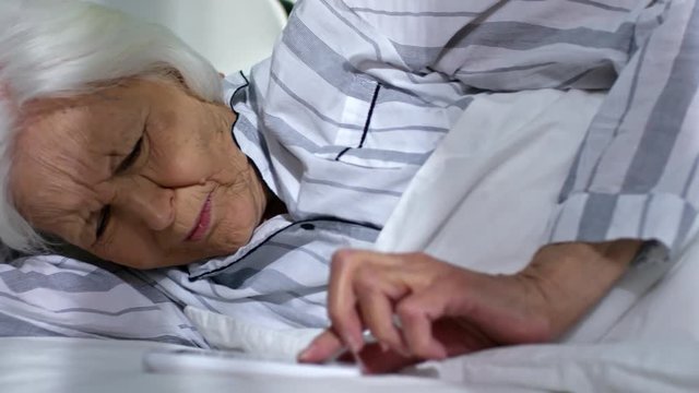 Medium shot of aged woman sleeping near aged man, turning off alarm clock on smartphone and continuing sleep