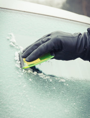 Naklejka premium Hand of man using green scraper to remove ice from window in car, winter problems