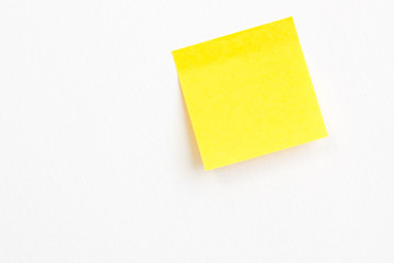 Yellow post it paper note on a white wall background with empty space.