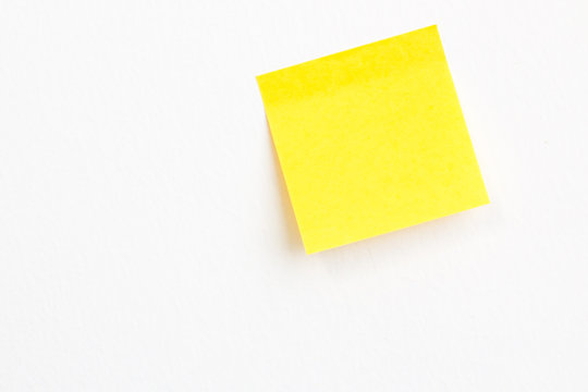 Yellow post it paper note on a white wall background with empty space.