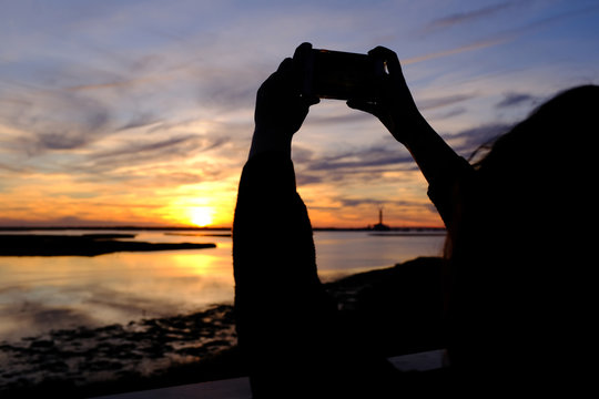 Person using phone to photograph sunset. 
