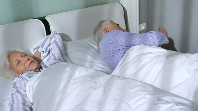 Tracking Left Of Aged Couple Sleeping In One Bed In The Morning, Checking Time In Watches And Continuing Sleep