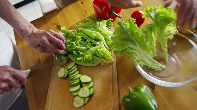 High angle view of hands of old people cutting vegetable salad and putting vegetables into big plate