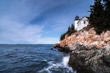 Fototapeta na wymiar white lighthouse over a blue ocean and red rocks with forest on the rocky coast of Maine under a blue sky