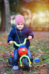 Cute little kid boy in warm autumn clothes having fun with tricycle.