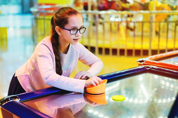 Young pretty girl in glasses with pigtails playing aero hockey on a slot machine.
