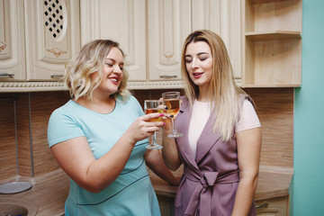 Two girlfriends women in the kitchen are having fun and drinking wine.