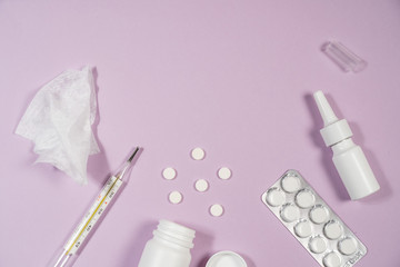 Various medicines, a thermometer, sprays from a stuffy nose and a pain in a throat on a pink background.