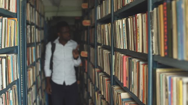 Black men picking book from one of the shelves at bookshop as present