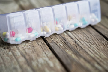 Variety of pills in white plastic pill organizer on weathered wood