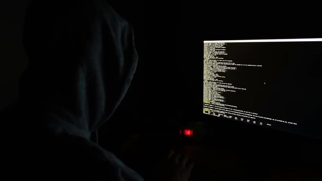 hacker in the hood programs the code in the dark, the command line on the monitor screen, 4k