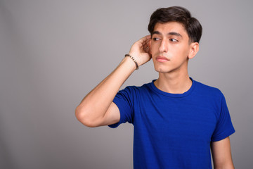 Fototapeta premium Young handsome Persian teenage boy listening against gray background