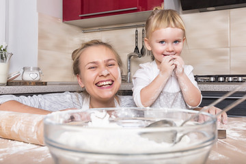 Happy family! A tiny daughter spends time with her mother in the kitchen to bake cookies. Mother's Day.