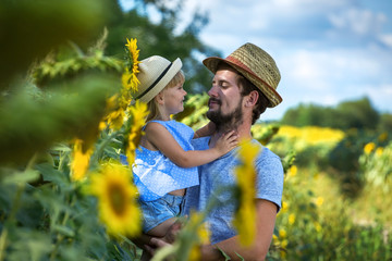 Father and daughter look at each other in the field of sunflowers.