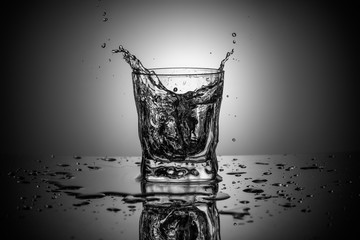 Black and white photofraphy of water splash in an elegant whiskey  glass on gradient background