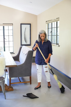 Mature woman cleaning at home, sweeping the floor with a broom