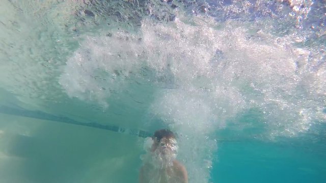 Underwater slow motion of young boy doing a cannonball into pool