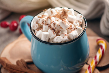 Mug of hot chocolate with marshmallow and a Lollipop stick on a knitted blanket background. Cozy warm winter composition