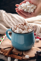 Hand throws marshmallow in a mug of hot chocolate on a wooden background. Cozy warm winter composition