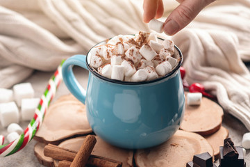 Hand throws marshmallow in a mug of hot chocolate on a wooden background. Cozy warm winter composition
