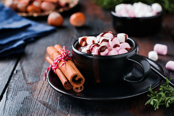 Hot chocolate with marshmallow candies in black ceramic cup on old dark vintage wooden background....