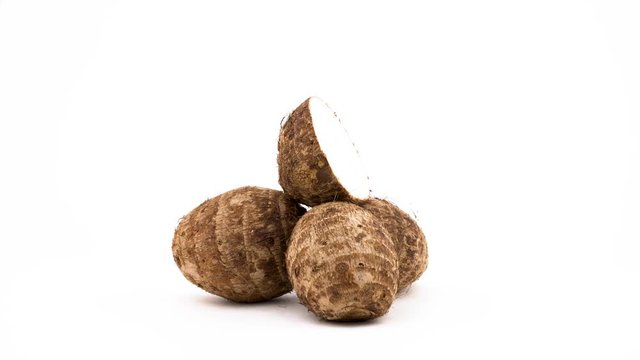 Three whole taro corms and one half cut. Rotating on the turntable. Isolated on the white background. Close-up. Macro.