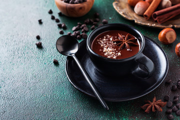 Hot chocolate with anise and nuts in black ceramic cup on old dark green concrete background....