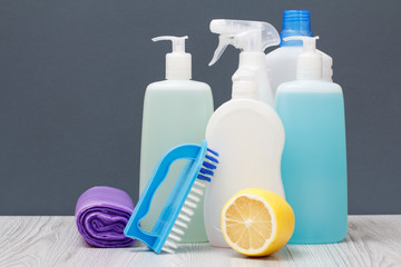 Bottles of dishwashing liquid, brush and lemon on gray background.